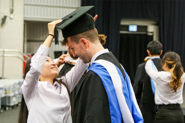 A student is fitted for a graduation hat in a robing room before the ceremony