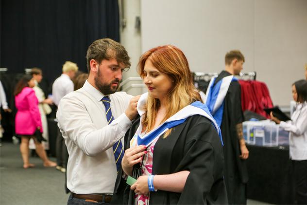 A student is fitted for a graduation gown in the robing room before a ceremony