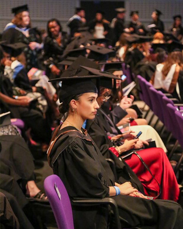 A student in a graduation gown sits waiting for a ceremony to begin