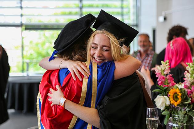An academic and a graduate embrace each other in a tight hug of happiness.