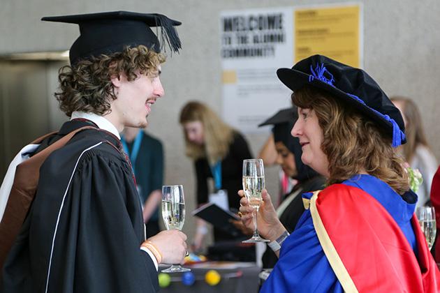 A male graduate talks to a Goldsmiths academic at the party while holding glasses of prosecco.