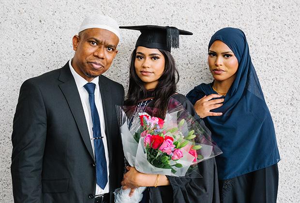 A grad holding flowers stands between her parents