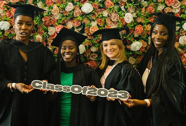 Four grads against a background of flowers holding a 'Class of 2023' sign