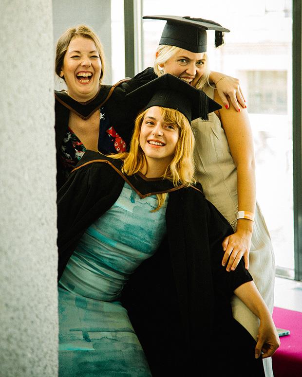 Three grads posing beside a pillar