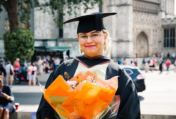 Grad looking at the camera holding an orange bouquet of flowers
