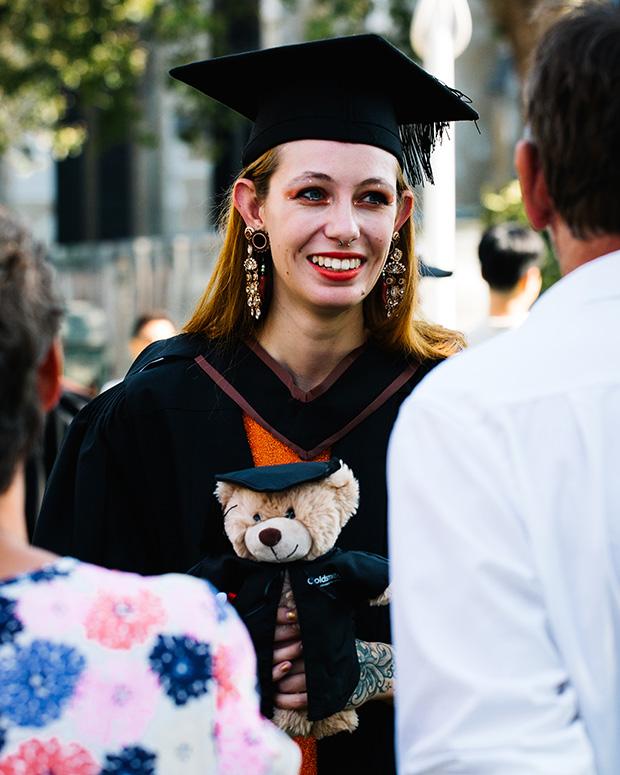 A grad standing holding a Goldsmiths teddy bear