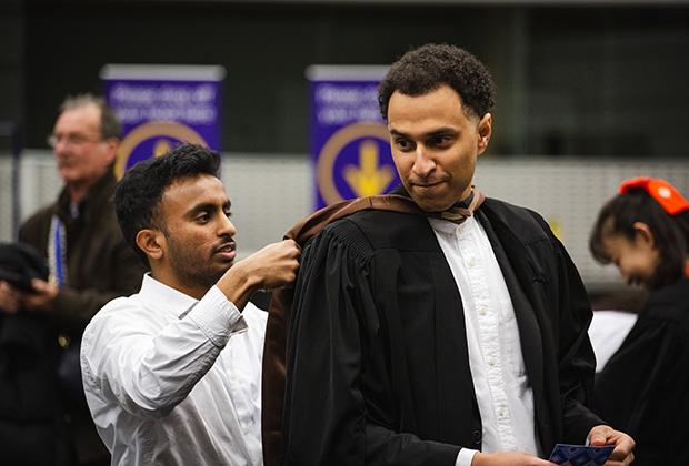 A graduand gets his gown fitted onto him
