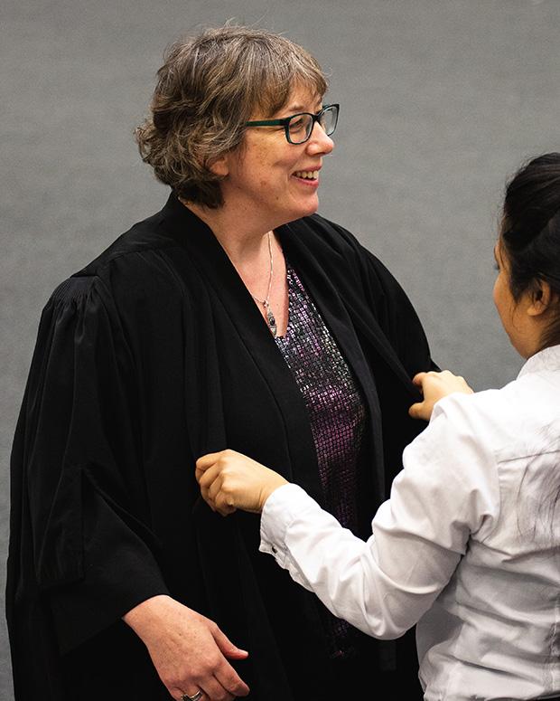 A graduand gets her cloak fitted on to her.