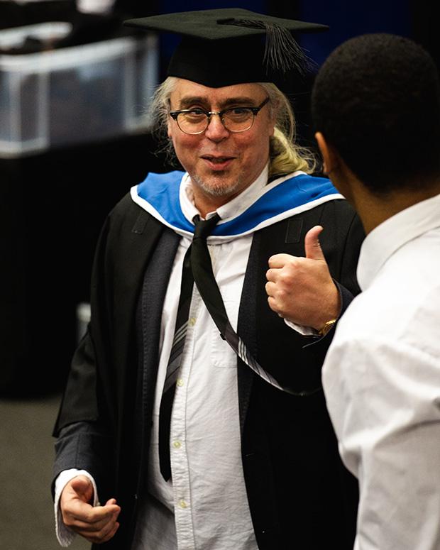 A graduand holds his thumb up to the person helping him fit his gown