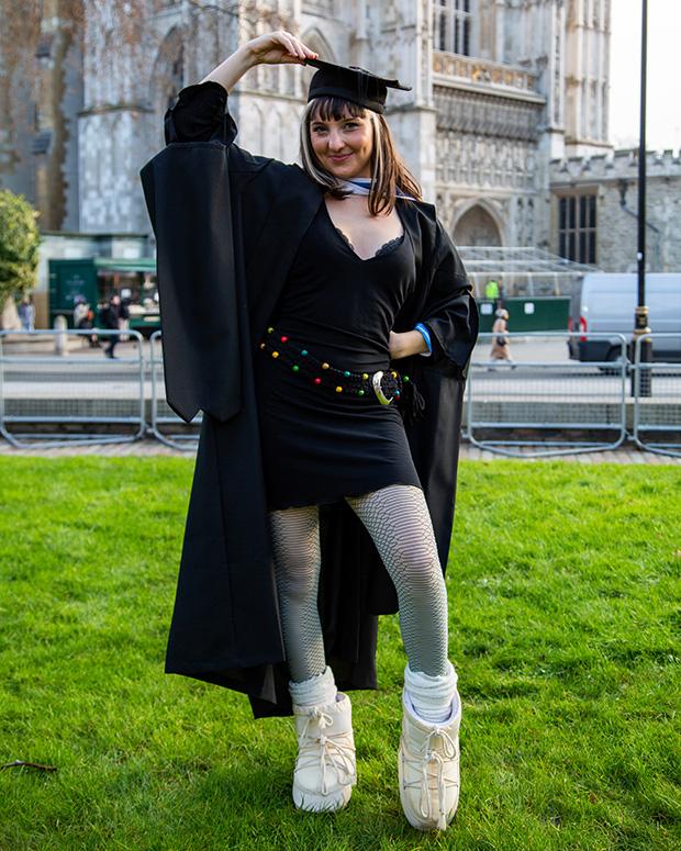 A graduate poses outside showing off her dress and big white moon boots