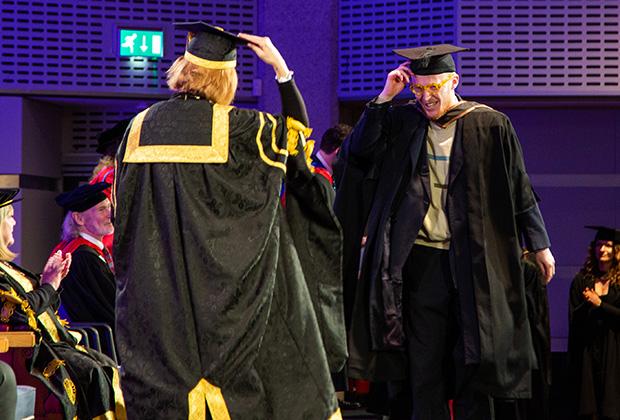 A graduate crosses the stage tipping his hat