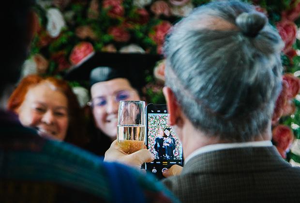 Over the shoulder of a guest taking a photo of graduates on a phone