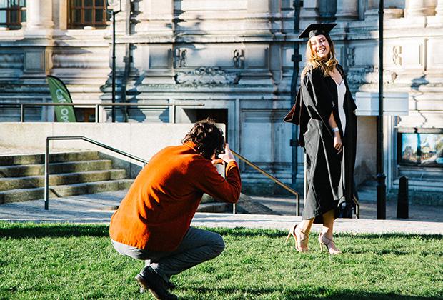 A graduate poses while a guest takes their photo