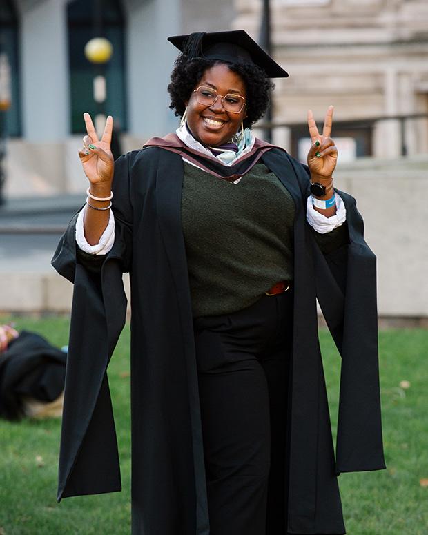 Graduate smiling holding her fingers in a victory sign