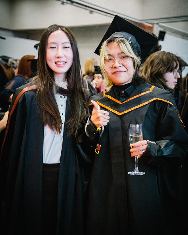 Two graduate friends at the reception, one holding up their thumb