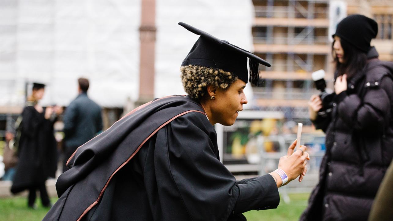 A woman wearing graduation robes takes a photo