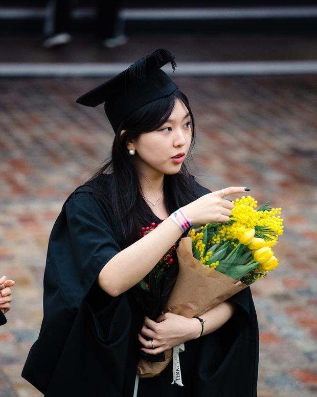 A woman posing with flowers outside their graduation ceremony.