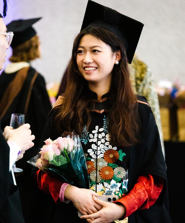 Graduate holds bouquet of flowers while smiling dressed in gown and hat 