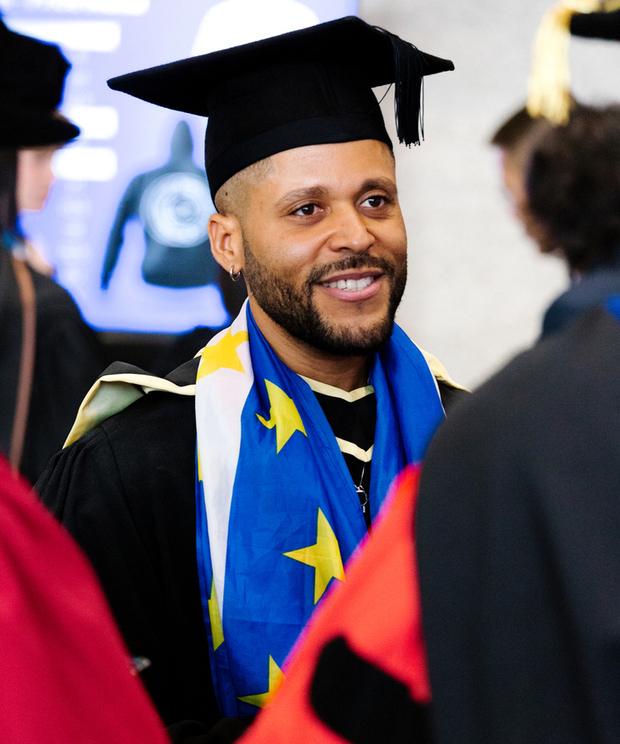 Male graduate wearing blue scarf with yellow stars in gown and hat