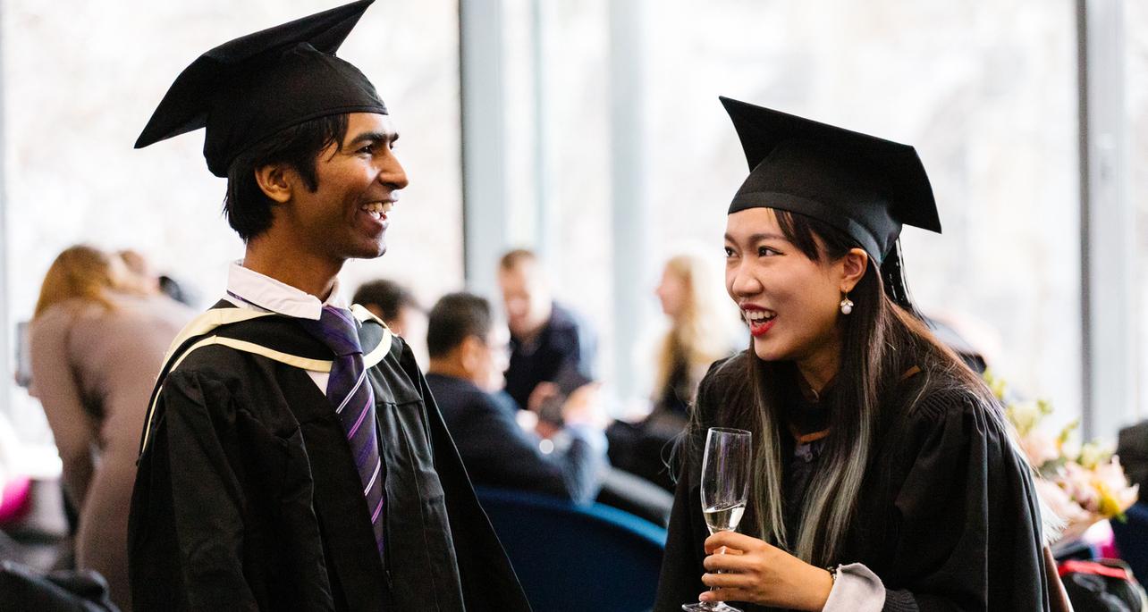 Two graduates, one male one female share a happy moment together, smiling and talking 