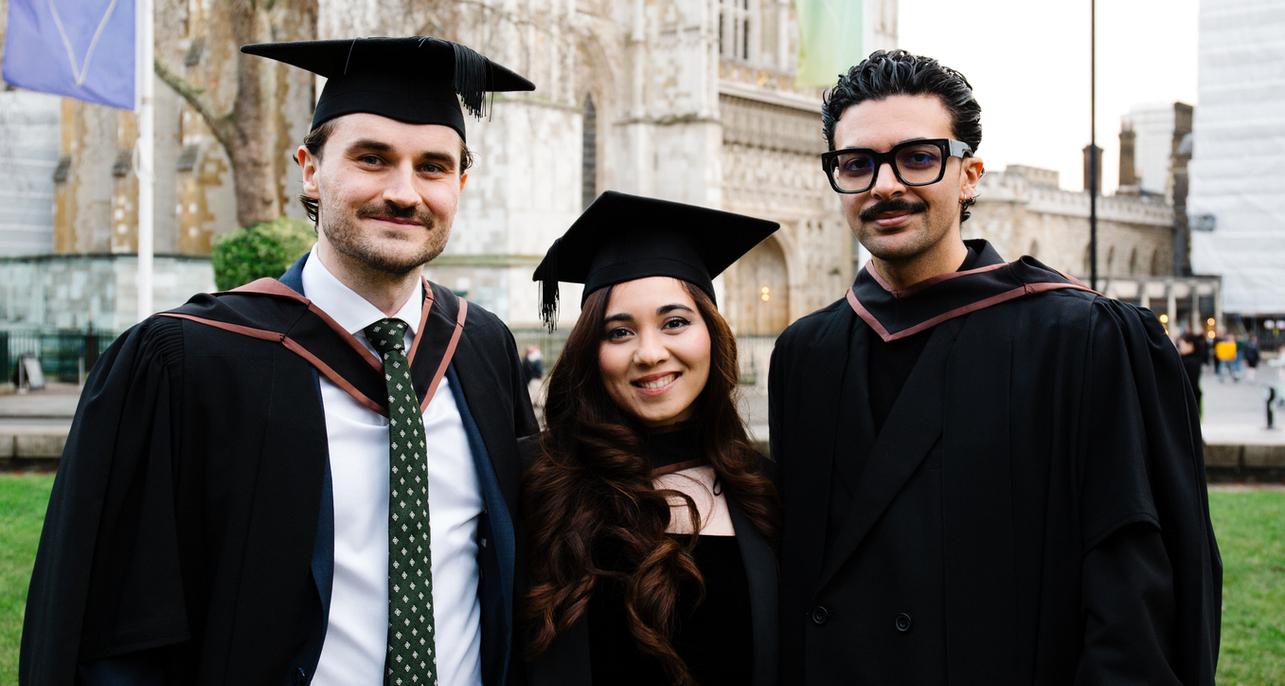 Three students, two male and one female pose for photographs outside of the building