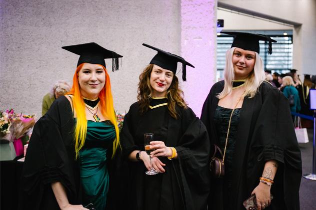 Three people pose for a picture in graduation gowns.