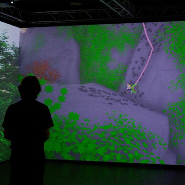 A person is silhoutted against a large screen displaying an interactive computer game.