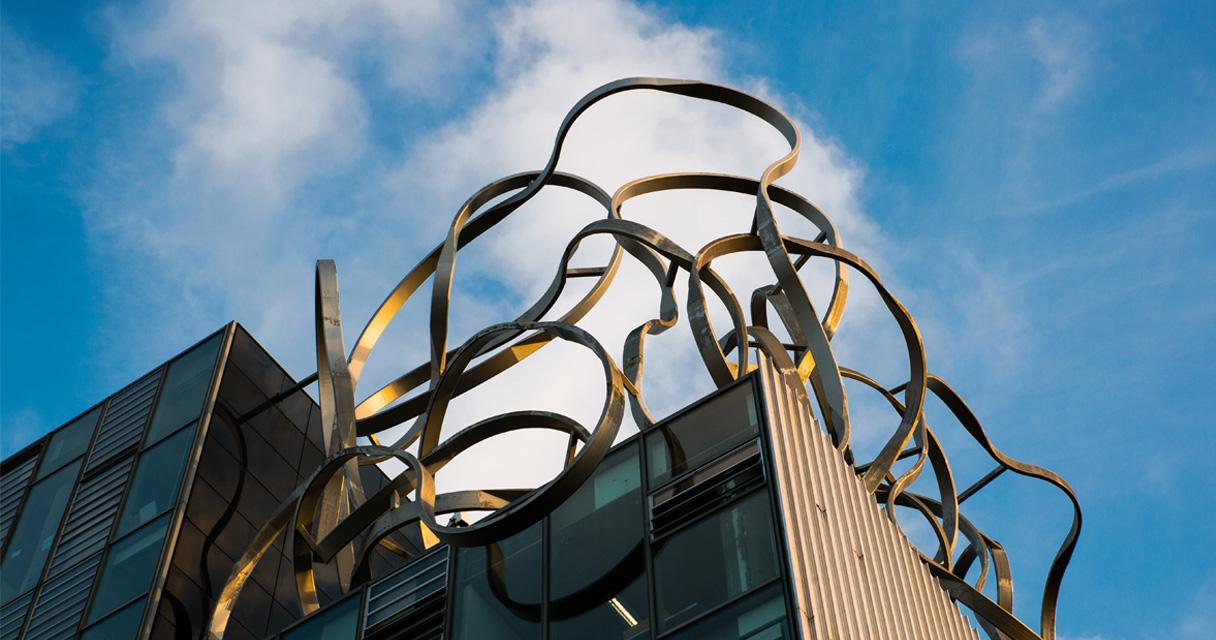 An image of a modern building with a metal sculpture against a blue sky.