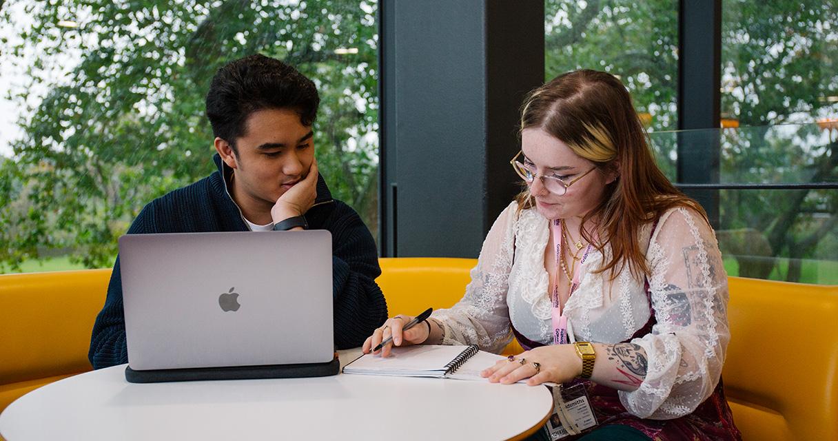 Students discussing work next to a laptop and notebook.