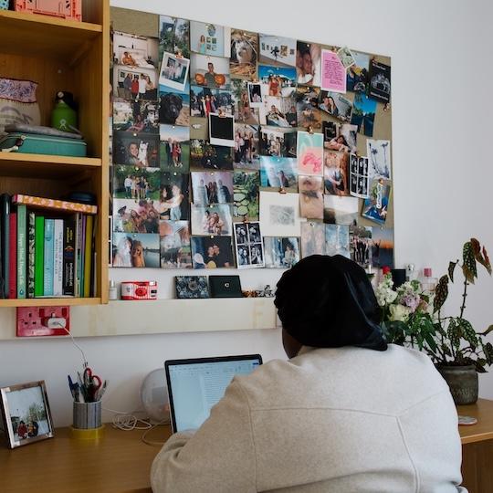 Student working at a desk with a picture board filled with photos in front of them.