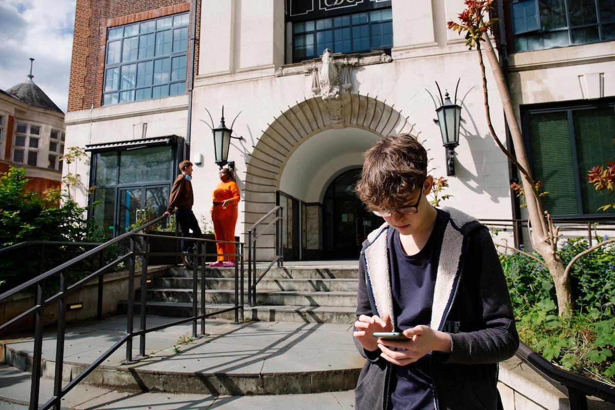 Student looking at their phone outside Town Hall Camberwell Accommodation with two students chatting in the background.
