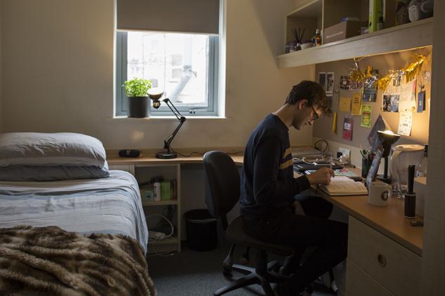 A male student sitting at a desk in his halls bedroom