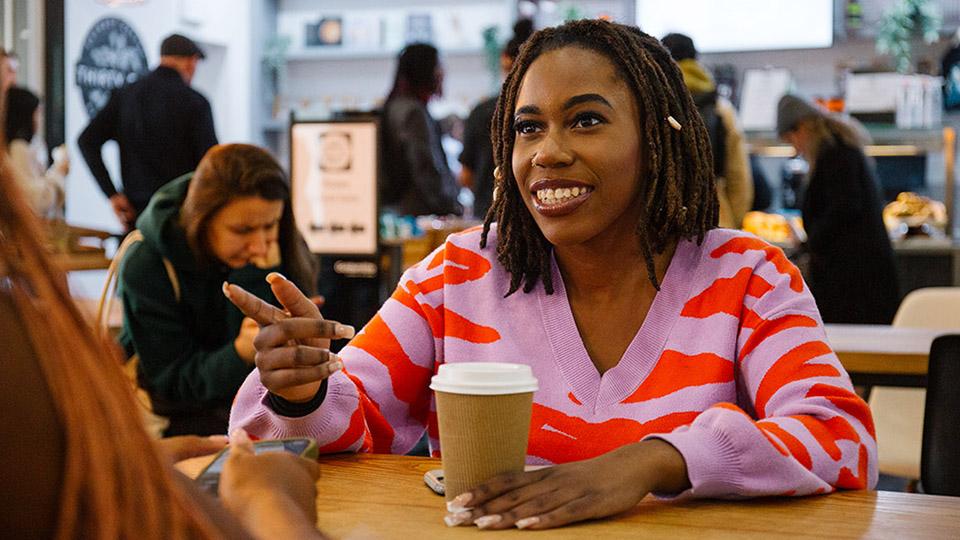 A student in conversation as they drink a cup of coffee