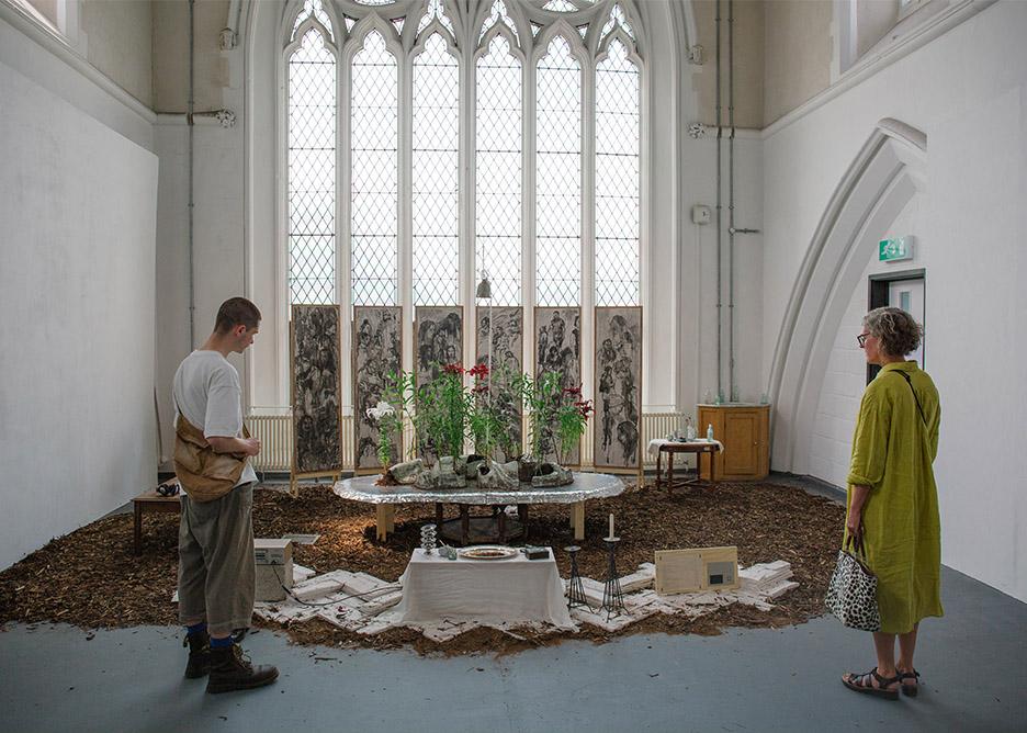 Two people looking at an art installation, with a large church window int he background