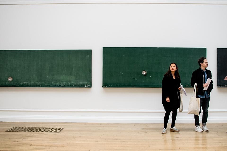 Two individuals standing in the South London Gallery looking at exhibition artwork
