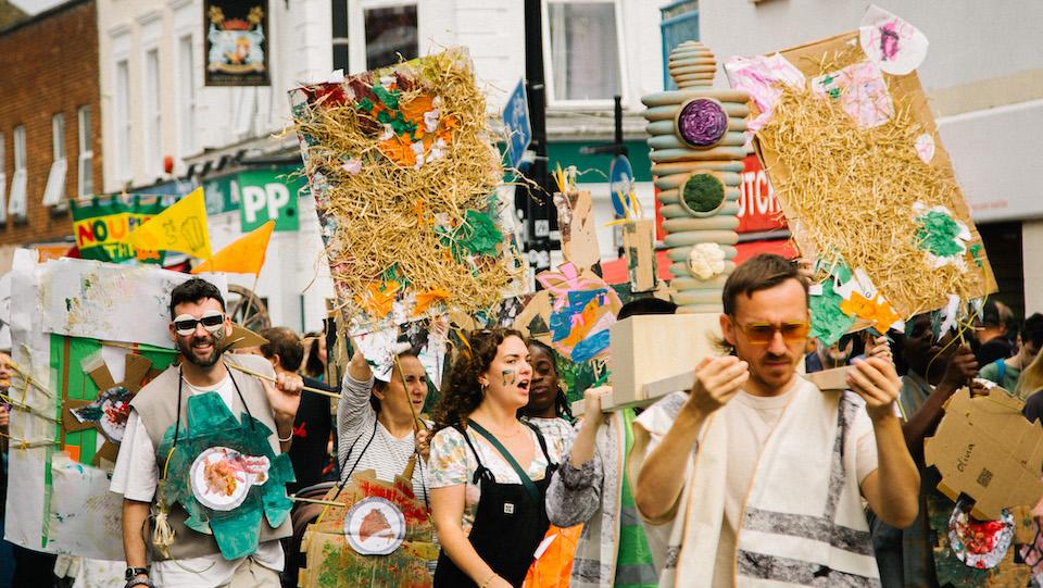 A group of people walking as part of a parade, wearing handmade costumes and holding handmade banners.