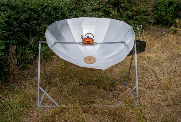 A kettle suspended over a large reflective sheet of metal to direct the sun's rays to boil water.