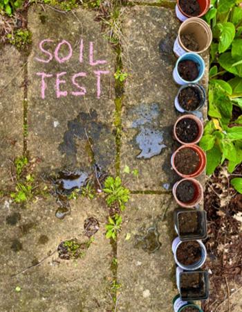 The words 'soil test' written on the concrete ground with a line of many small pots containing soil.