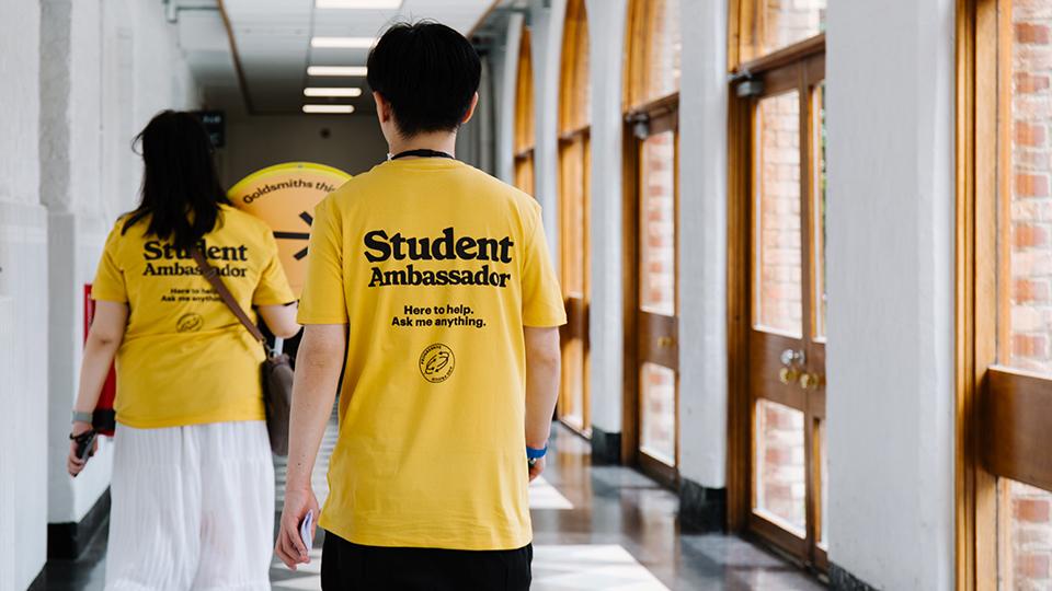 Student ambassadors walking down a corridor, with their t-shirts reading 'Student ambassador. Here to help. Ask me anything'