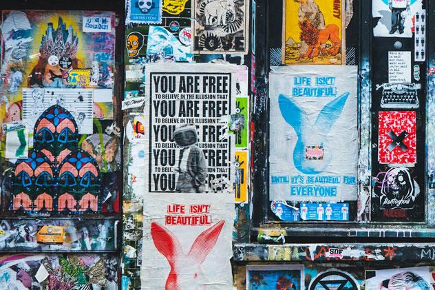 Close-up of grafitti and fly posting on a wall in London's Brick Lane, including a poster saying 'You are free to believe in the illusion that you are free'
