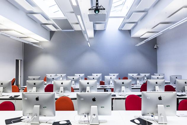 A Goldsmiths computer suite, featuring rows of shiny iMac computers, interspersed with red chairs.