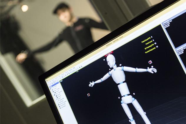 A close-up of a computer screen showing human motion capture points, with a person holding their arms out in the background.