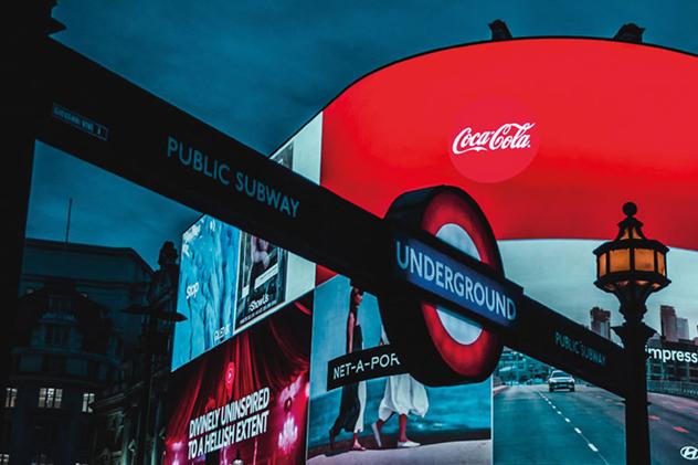 London's Piccadilly Circus by night, featuring a London Underground sign in the foreground and big neon screens in the background