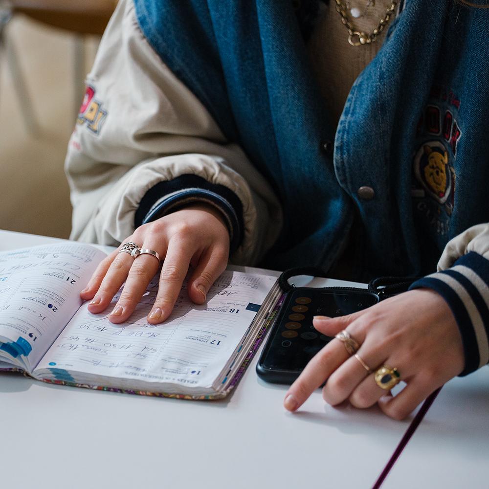 A student with a notebook and calculator open on their phone.