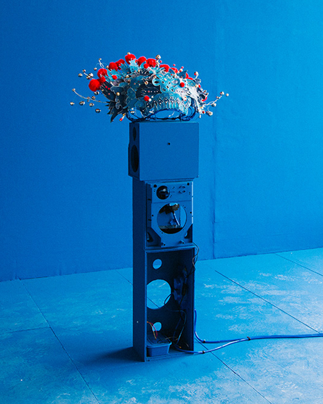 A blue mechanical-looking sculpture sits against a completely blue backdrop.
