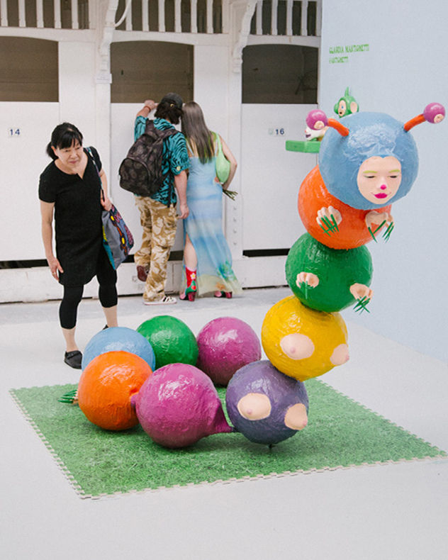 A large caterpillar-like sculpture formed from colourful spheres, with a human face. A woman looks at the sculpture.