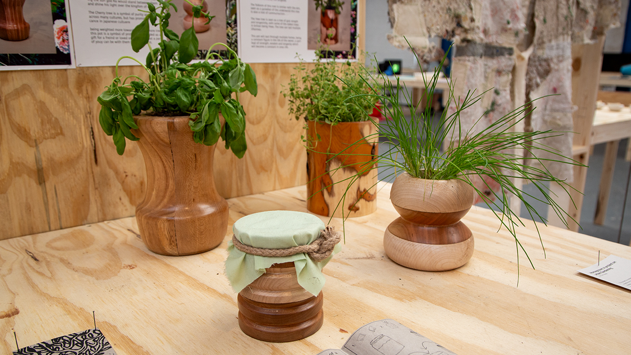 A series of four wooden vases and vessels sitting on a table. Each vessel holds a plant.