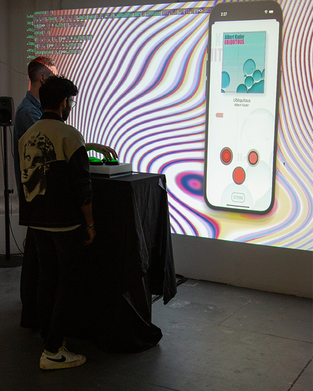 Two people interact with a game playing on a large screen. The two people are pressing large green buttons that sit on a table in front of them.