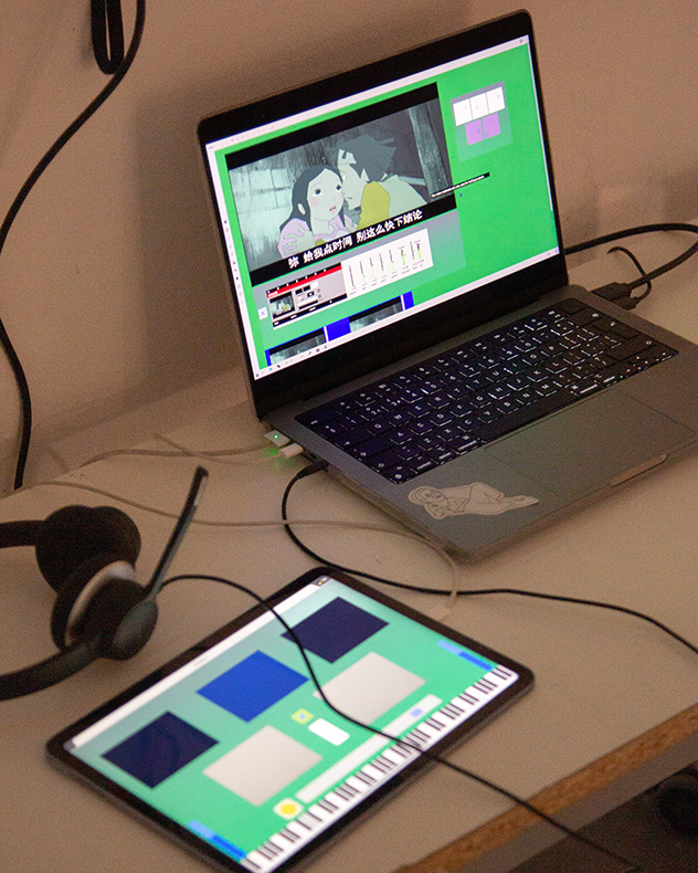 A laptop, tablet and headphones on a white table. The laptop shows an animation on a green backdrop, whilst the tablet shows a piano keyboard and a series of blue and grey rectangles.